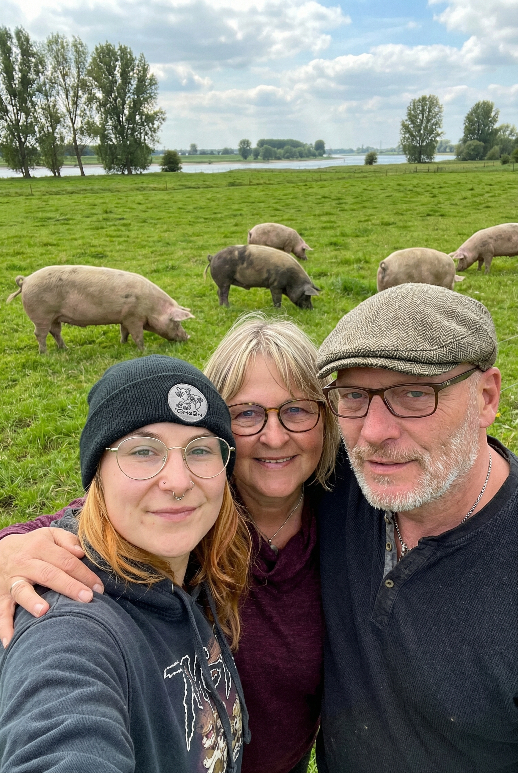 Drei Menschen stehen zusammen auf einer Weide, hinter ihnen grasen mehrere Schweine.
